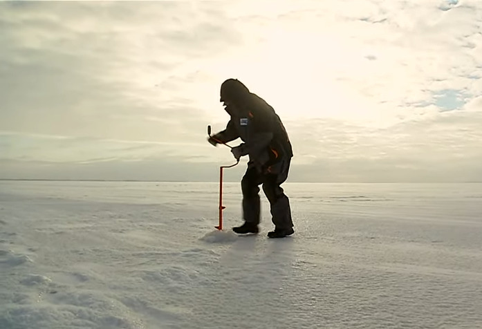 Рыбак делает лунку на льду с помощью ледобура