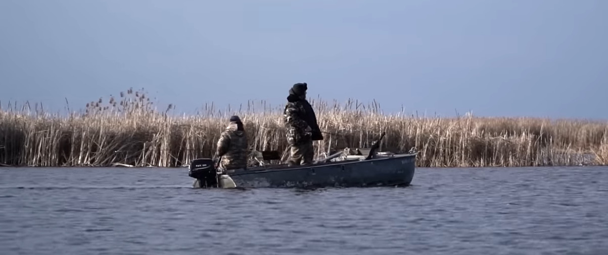 Два рыбака на лодке с мотором на воде в зимней одежде