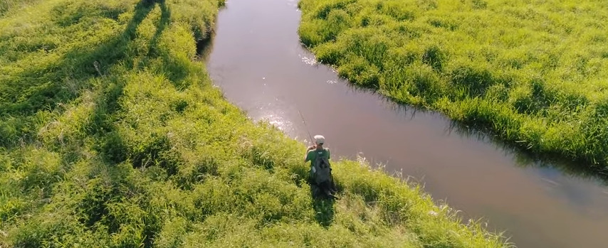 Рыбак со спиннингом сидит на травянистом берегу реки