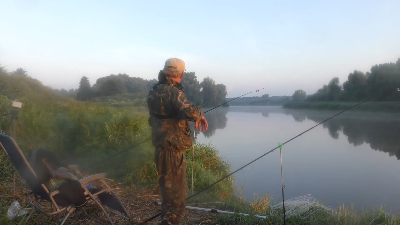 Рыбак стоит на берегу реки рядом с установленным снаряжением и снастями