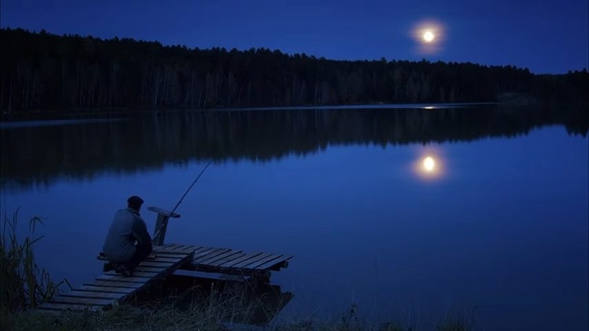Рыбак сидит ночью на берегу с удочкой